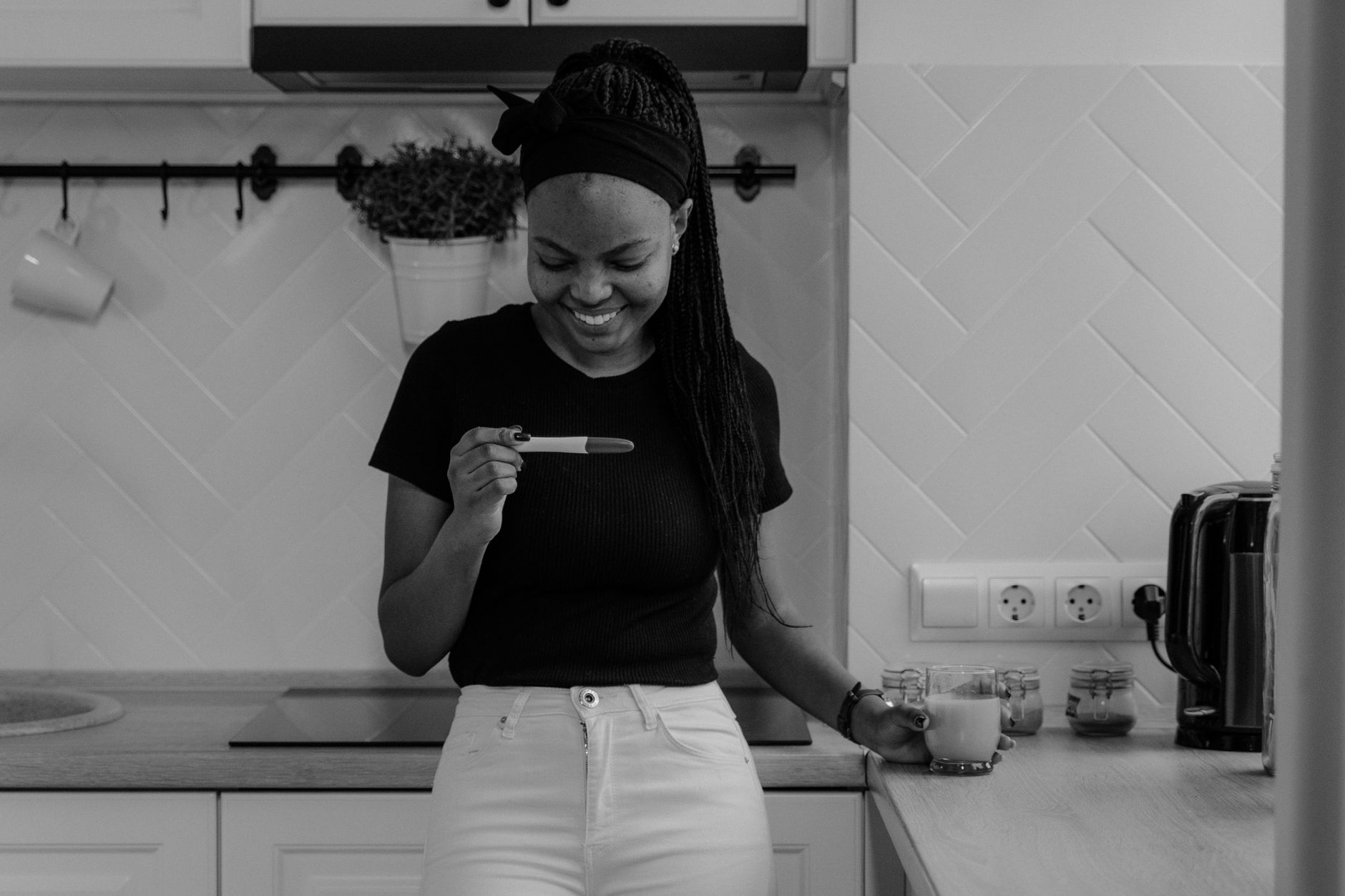 Pregnant woman in cosy kitchen reaching for pickles + chocolate on the counter
