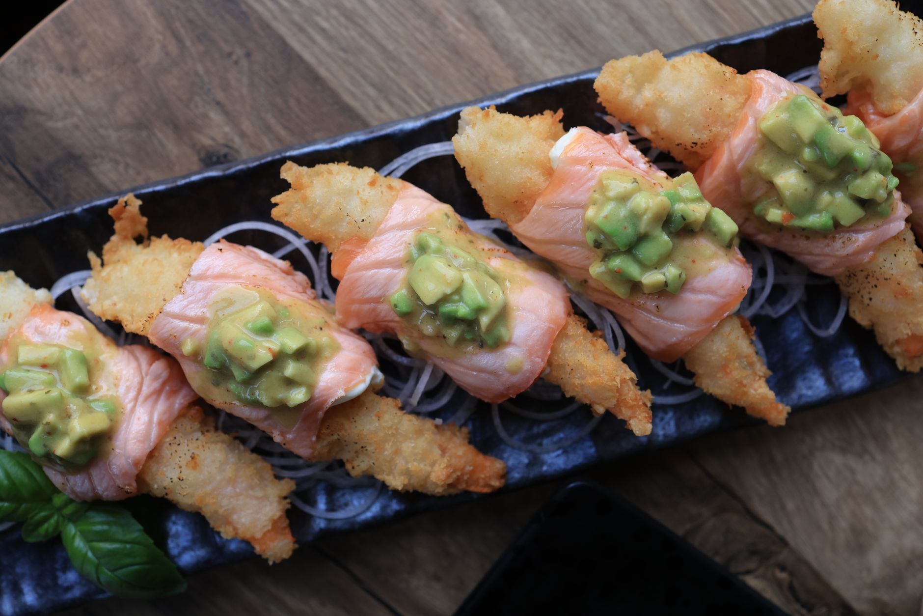 Salmon, prawn tempura + avocado sushi rolls on a wooden board